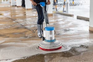 Worker cleaning sand wash exterior walkway using polishing machine and chemical or acid